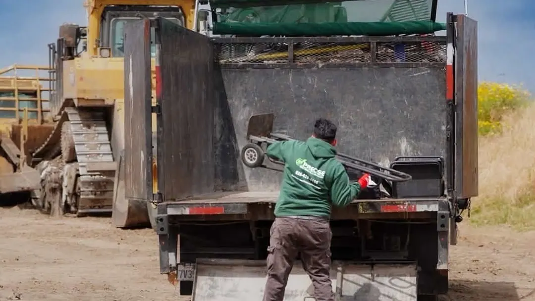 A crew member lifting a hand truck onto the back of the dump truck