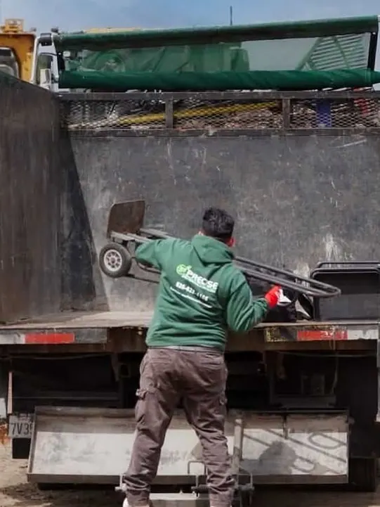 A crew member lifting a hand truck onto the back of the dump truck