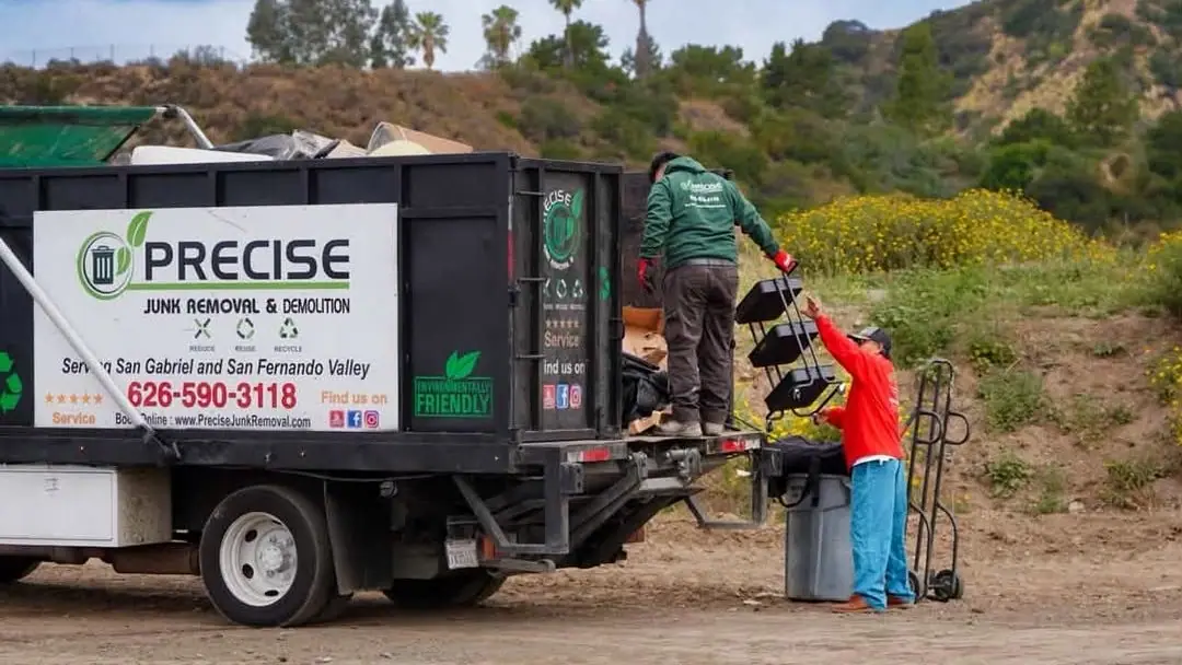 Two crew members loading junk onto the truck on a dirt track below a hillside