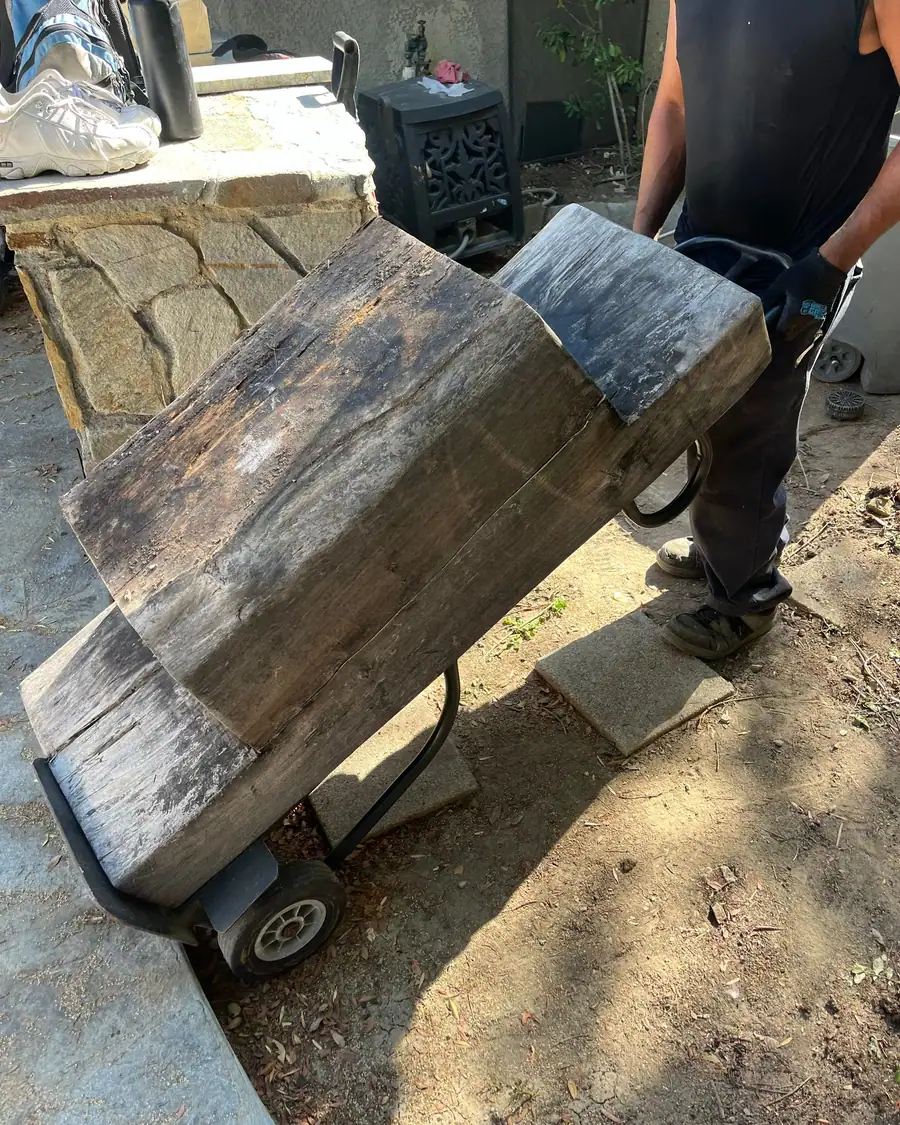A crew member wheeling two heavy weathered beams out on a hand truck