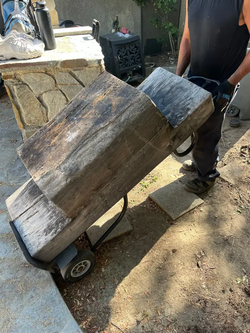 A crew member wheeling two heavy weathered beams out on a hand truck