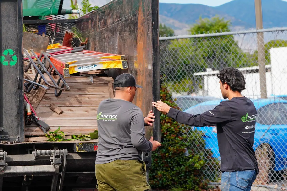 Two of the crew swinging the truck gate shut on a load of scrap metal and a ladder