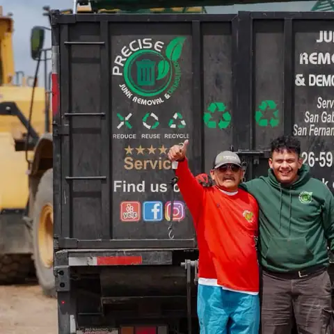 Two crew members standing at the open rear gate of the loaded dump truck