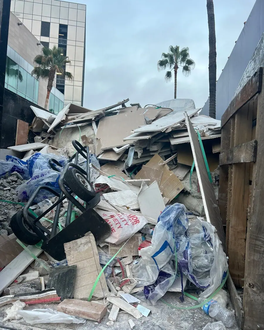 A large pile of broken timber and bagged debris beside a house wall