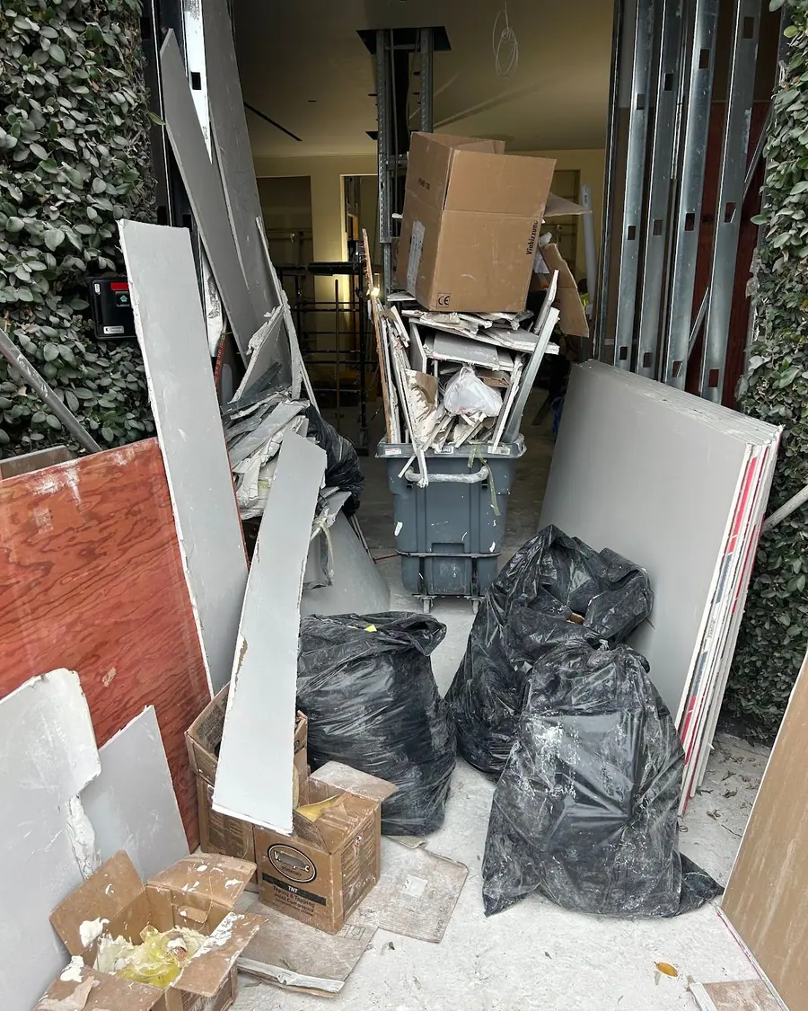 Lengths of drywall and bagged debris stacked against a garage wall