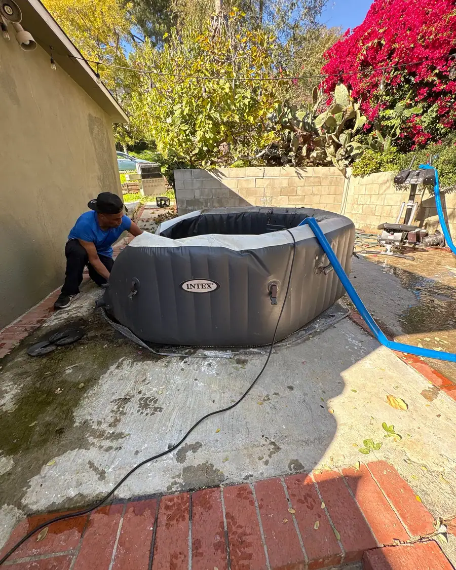 A crew member folding down an inflatable hot tub after draining it, the drain hose still running
