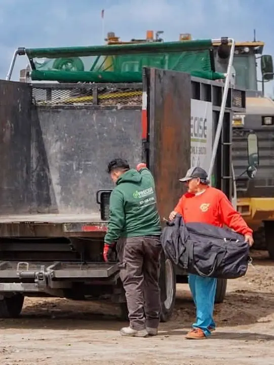 Two crew members lifting a large black bag off the back of the truck