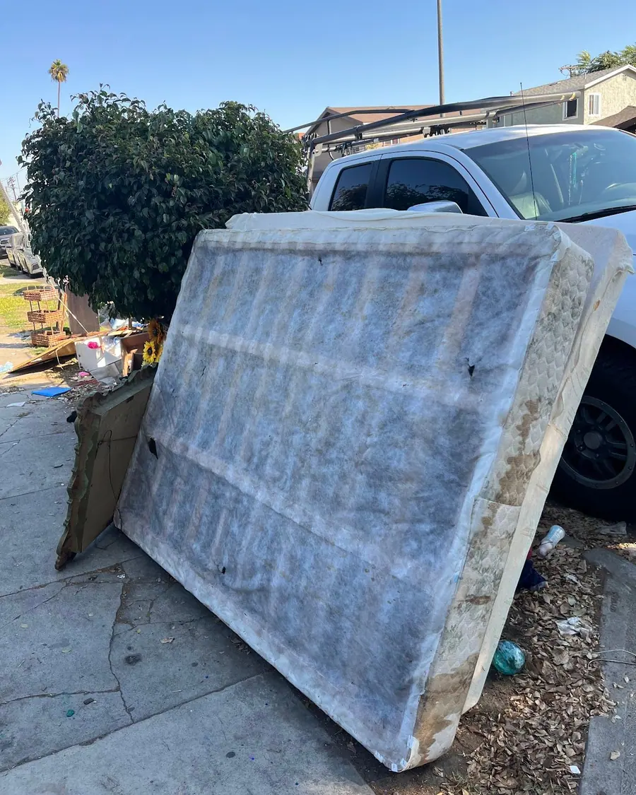 A worn mattress set out at the curb next to a pickup, waiting to be loaded