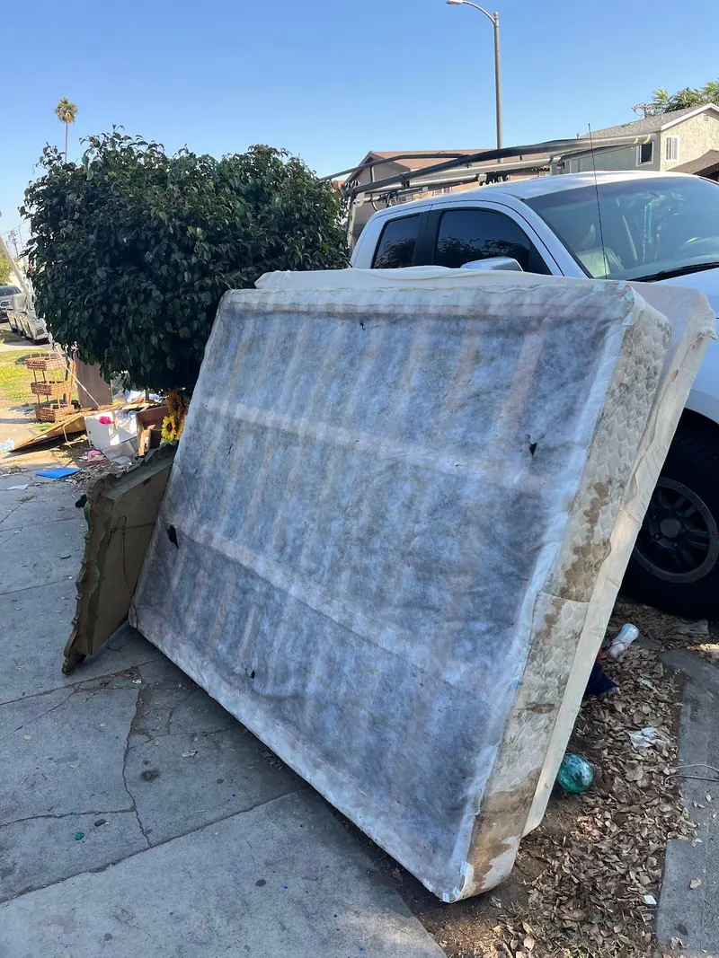 A worn mattress set out at the curb next to a pickup, waiting to be loaded