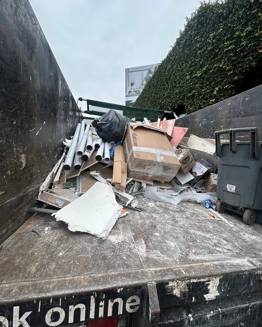 Mixed household and building debris piled beside a dumpster