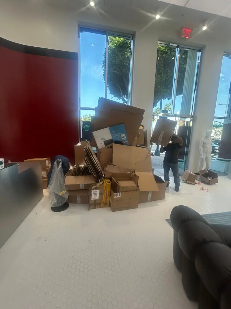 A crew member carrying a flattened box out of a store, a pile of cardboard behind him
