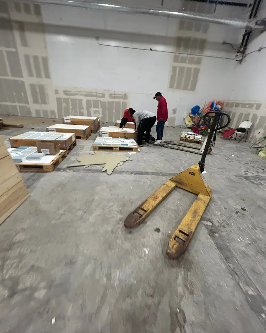 Three crew members working crates on pallets across an empty warehouse floor